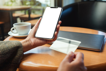 Mockup image of a hands holding credit card and a mobile phone with blank desktop screen in office