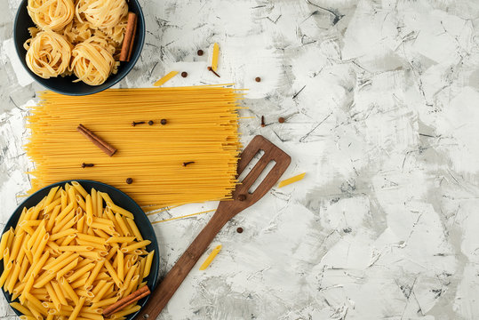 various dry pasta in blue dishes and spiced spaghetti on a mottled gray textured background