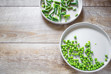 Green vegetables, peas and asparagus, served on two white plates on wooden table. Rustic food background, copy space, flatlay. 