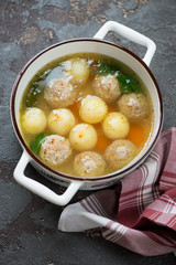 Meatball and potato soup in a white bowl, elevated view on a brown stone surface, vertical shot