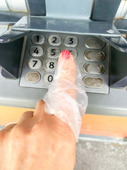Fototapeta premium Coronavirus and cash. Woman presses a finger on an ATM. Using a plastic bag or gloves on your hand to avoid viruses, germs, bacteria from dirty ATM buttons.