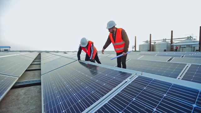 Enginneers installing new sunny batteries. Two workers in a uniform and hardhat installing photovoltaic panels on a solar farm.