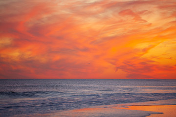 Commercial airplane approaching its destination over a beach during a vibrant pink and orange sunset. 