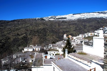 General view over town rooftops towards the snow capped mountains, Bubion, Spain.