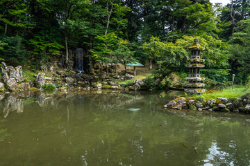 Fototapeta na wymiar Small waterfall and stone lantern on the near the Hisagoike pond at Kenrokuen garden, Kanazawa, Japan
