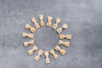 Homemade pasta in the form of bows is laid out on a circle on a gray surface. Top view.