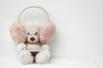 Teddy bear in pink headphones with smart phone on a white background