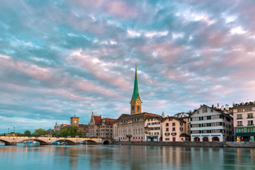 Fototapeta premium Famous Fraumunster church with its reflections in river Limmat at pink sunrise in Old Town of Zurich, the largest city in Switzerland