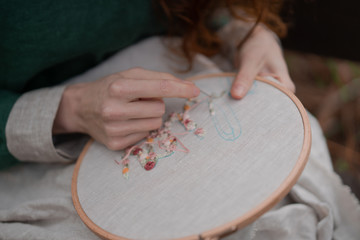 Hands of girl / woman / female in boho linen dress hold sewing stitching pattern in embroidery...