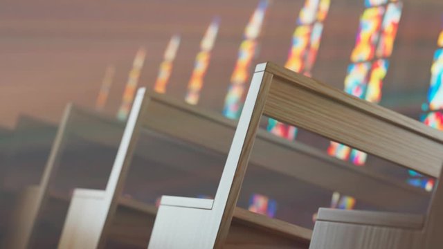 Endless rows of church benches lit by the sun through a stained glass window.