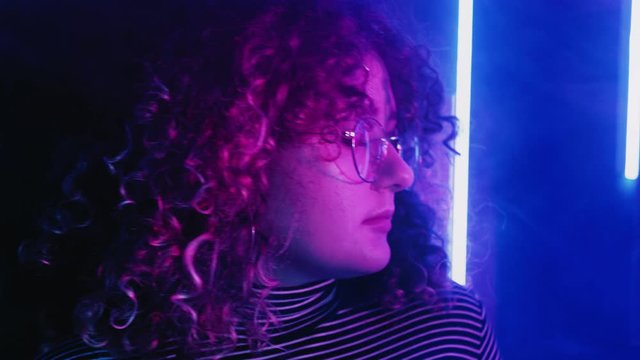 Colorful light face. Sweet memories. Relaxed girl with curly hair in blue pink neon illuminated haze.