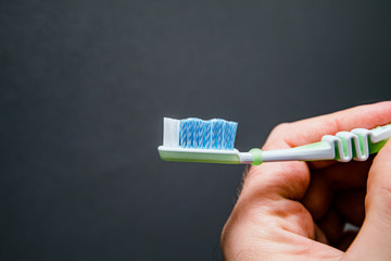 Close-up male hand holding new toothbrush against gray background