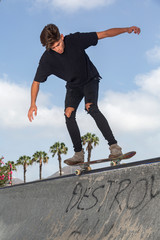 Young skateboarder performing tricks in a park, with street background and blue sky.