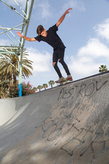 Young skateboarder performing tricks in a park, with street background and blue sky.