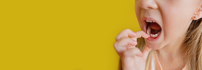 Kid dropped the first milk tooth. Change teeth concept. Cute little girl with blonde hair on yellow background with copy space. Horizontal banner for web design