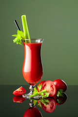 Tomato juice with celery on a black reflective background.