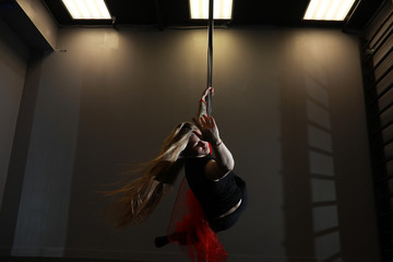 The dancer on the pylon in the studio. Girl doing exercises on a sports equipment.