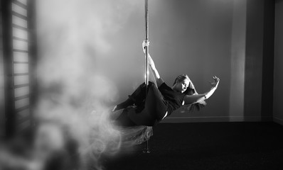 The dancer on the pylon in the studio. Girl doing exercises on a sports equipment.