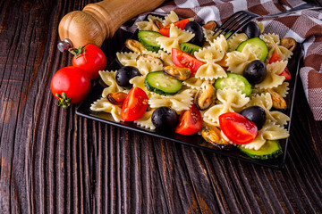 Delicious pasta salad with tomato cucumber and olives on wooden rustic background