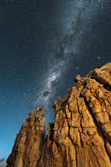A beautiful vertical night sky landscape, with a yellow rock formation in the foreground and the Milky Way against a deep blue sky in the background, taken in the Cederberg mountains, South Africa.
