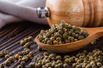 green peppercorns in wooden scoop on rustic background