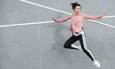 Obraz premium An athletic young woman is jumping, doing acrobatics, ballet, is actively involved in sports, against a concrete wall.