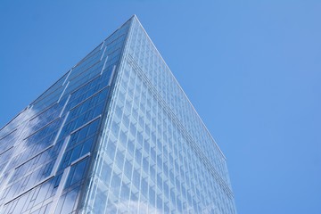 Modern curtain wall made of glass and steel. Blue sky and clouds reflected in windows of modern office building. 