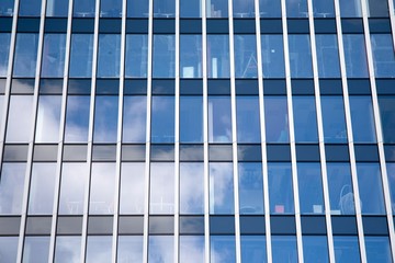 Modern curtain wall made of glass and steel. Blue sky and clouds reflected in windows of modern office building. 