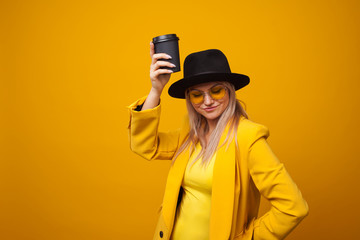 Take-away coffee. Stylish trendy young woman in bright clothes on a yellow background.