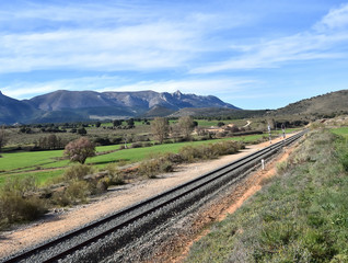 Fototapeta na wymiar Train track crossing a beautiful landscape with meadows, trees and mountains in Andalusia