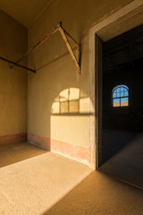 A vertical photograph inside an abandoned house with an open doorway leading into another room and a shaft of golden light streaming in the room, taken in the ghost town of Kolmanskop, Namibia.