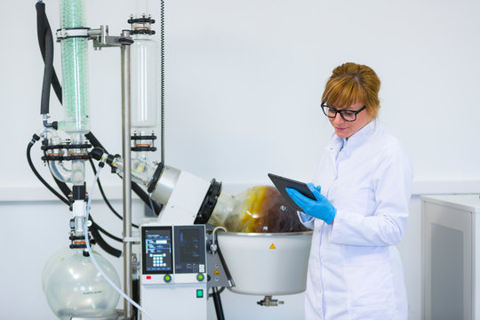 Chemist working on tablet next to rotavapor machine in laboratory