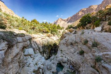 Fototapeta na wymiar Wadi Tiwi real water spring and waterfall, Oman - Water spring, waterfall and eroded canyon surrounded by palm trees oasis in Oman.
