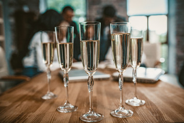 Five Champagne Glasses Standing On Negotiation Table At Business Event, Team Of Coworkers Celebrating Agreement Or Successful Project In Office On Blurred Background, Toned Image