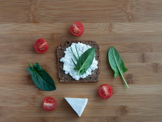 Sliced rye bread with cottage cheese and vegetables on wooden table