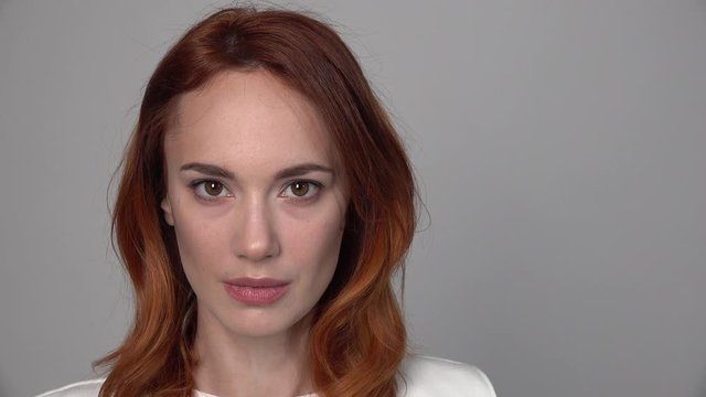 Beautiful red-haired girl slowly raises her eyes in front of the camera, her head is large enough against a neutral background