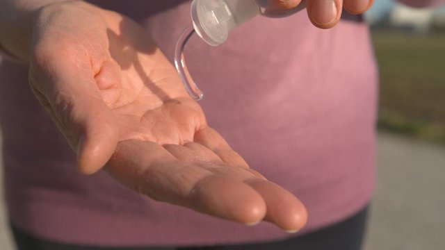 SLOW MOTION, CLOSE UP: Unrecognizable woman squirts a dab of hand sanitizing gel into her palm to cleanse her hands during the COVID-19 pandemic. Caucasian female using alcohol hand disinfectant.