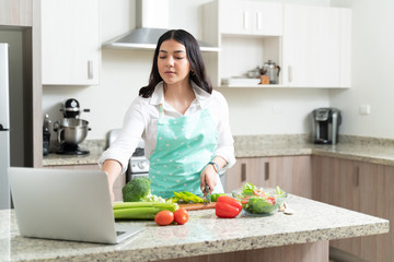 Caucasian Housewife Cutting Bell Pepper While Using Laptop