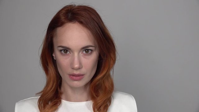 Beautiful red-haired girl slowly raises her eyes, then raise one brow,  in front of the camera, her head is large enough against a neutral background