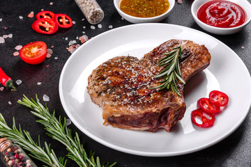 Fresh delicious juicy steak on the bones with vegetables and spices against a dark background