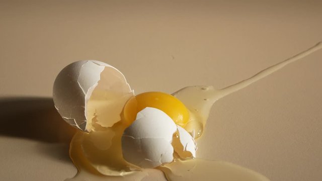 A chicken egg falls from a height onto a table and breaks. The shell breaks, the yolk and protein spread over the surface
