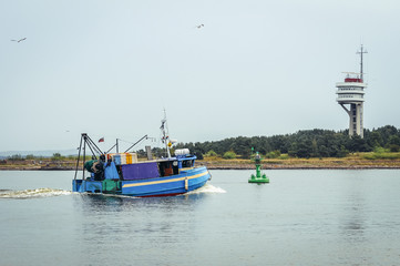 Naklejka premium Fishing boat and control tower in port of Swinoujscie, coastal city over Baltic Sea, Poland