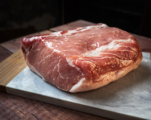 Raw piece of pork lies on the kitchen board, lying on a wooden table