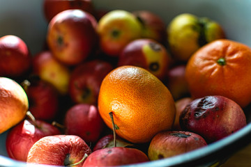 Bright juicy fruits, natural and natural fruits   with damage. Red apples and tangerines in a Cup   with sun rays