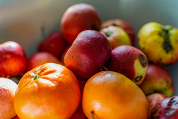 Bright juicy fruits, natural and natural fruits   with damage. Red apples and tangerines in a Cup   with sun rays