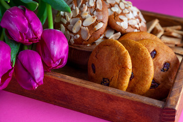 A tray with cookies and pink tulips on a pink background. Round homemade cookies with almonds and lingonberries. Delicious pastries, snack. Flour product, food.