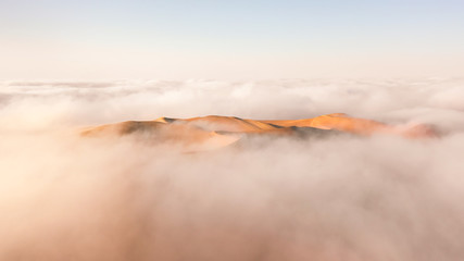 Aerial view of a massive sand dune surrounded by winter morning fog cloud in Empty Quarter. Liwa...