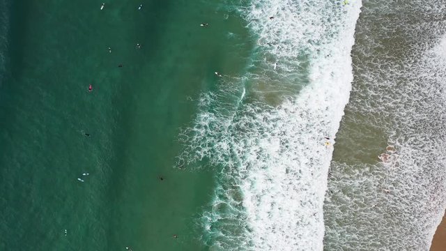 Praia da Arrifana in west Portugal with Surfers seen from above riding waves, Aerial top view rotating shot
