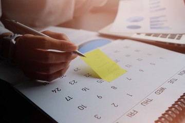 Asian woman is writing something on yellow paper note or calendar to remind the meeting, data preparation, take appointment protect for mistake or get information for shopping online. work at home