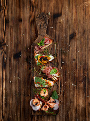 Assorted bruschetta set on a wooden platter: with pear and parma ham, salmon and cheese, baked pumpkin and ricotta cheese